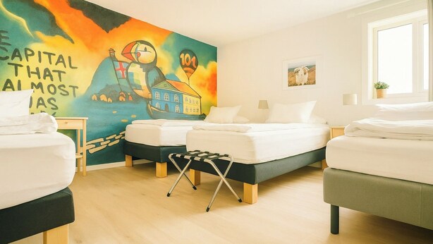A hotel room with two beds, a wooden floor, a colorful mural, and a window with a view. - Stykkisholmur Inn (Stykkisholmur)