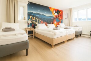 Camera d'hotel con un letto grande, un letto più piccolo, un divano e un comodino. Si vede una finestra con vista sulla città e una parete decorata con un murale colorato.