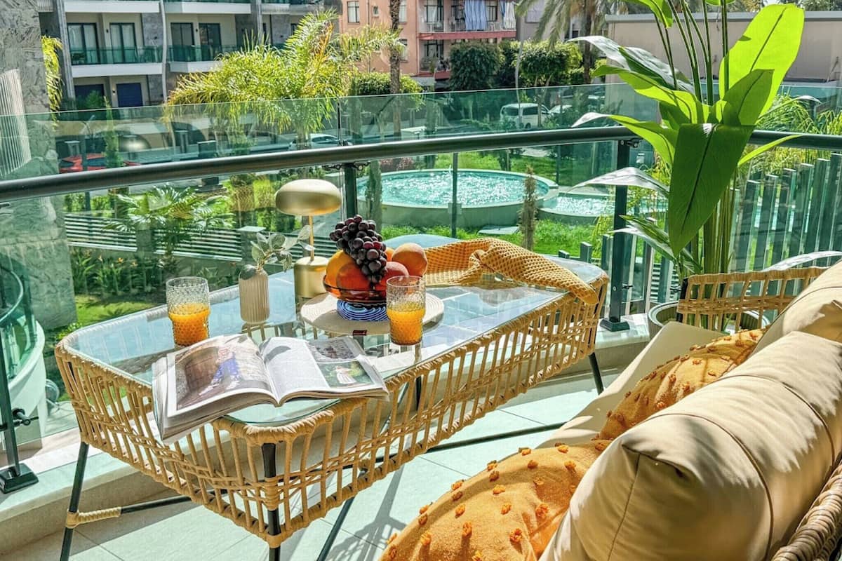A balcony with a glass table, wicker chairs, a sofa, and a view of a cityscape.