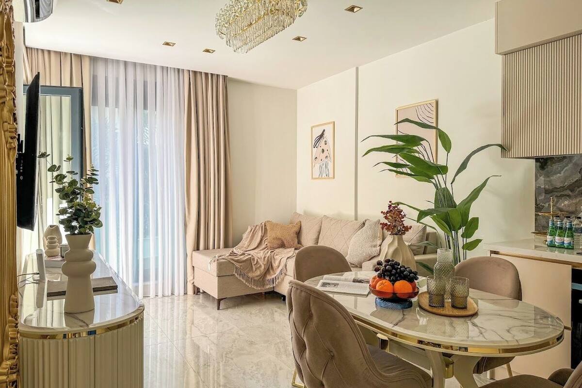 A modern living room with a sofa, a dining table with fruit, and a large plant.