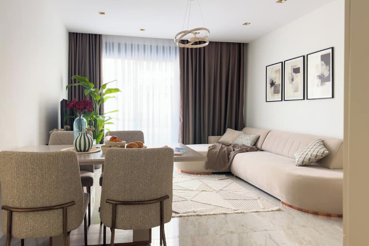 A modern living room with a sofa, a dining table with chairs, and a large window with curtains.