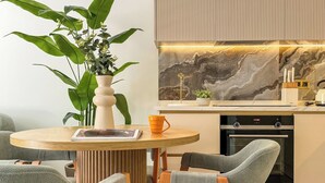 A modern kitchen with a marble backsplash, a built-in oven, and a dining area with a round wooden table and grey upholstered chairs. - Qoople Legends (Alanya)