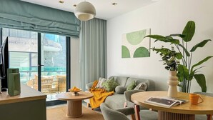A modern living room with a sofa, chairs, a coffee table, and a dining area with a table and chairs. There is a large window with curtains, a plant, and artwork on the wall. - Qoople Legends (Alanya)