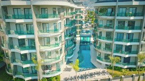A multi-story hotel with balconies, a central swimming pool, and outdoor seating areas. - Qoople Legends (Alanya)