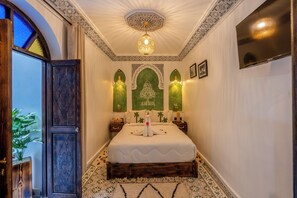 A bedroom with a large bed, decorative wall sconces, a chandelier, and a TV mounted on the wall. - Riad La Perle Bleue (Marrakech)