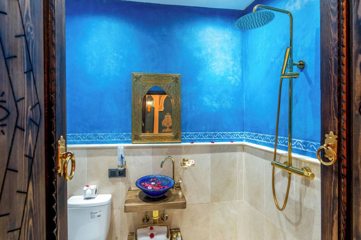 Un bagno con parete blu, un lavandino con bacinella azzurra, una doccia e un water.