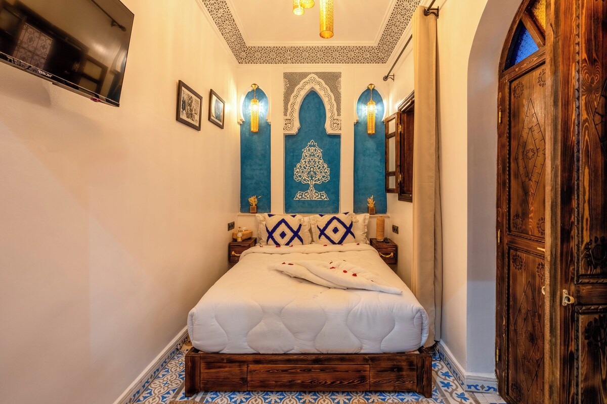 A bedroom with a large bed, a wooden wardrobe, and a TV mounted on the wall.