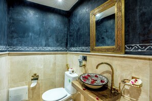 A bathroom with a white toilet, a sink with a decorative basin, and a gold-framed mirror. - Riad La Perle Bleue (Marrakech)