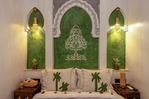 Une chambre comprenant un lit, deux tables de chevet, un mur décoratif orné d’un motif d’arbre et deux lampes fixées au mur.