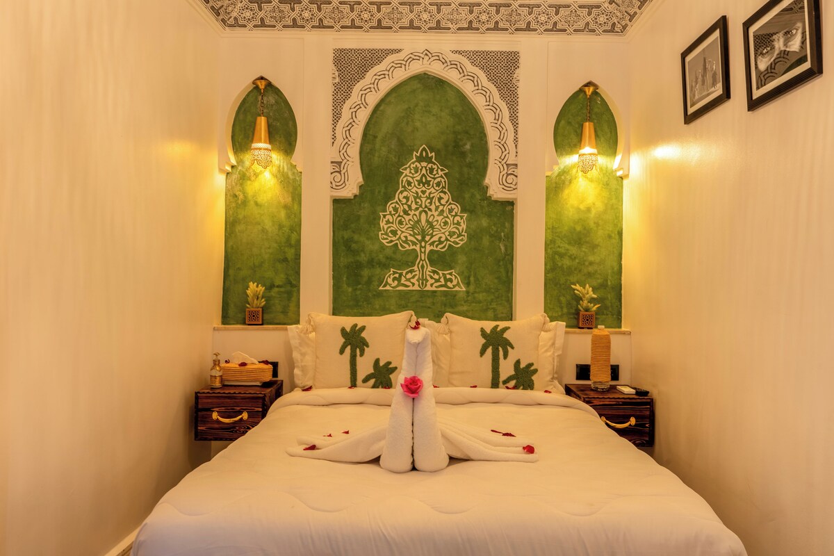 A hotel room with a bed, decorative pillows, a wall with a green design, and two nightstands with lamps.