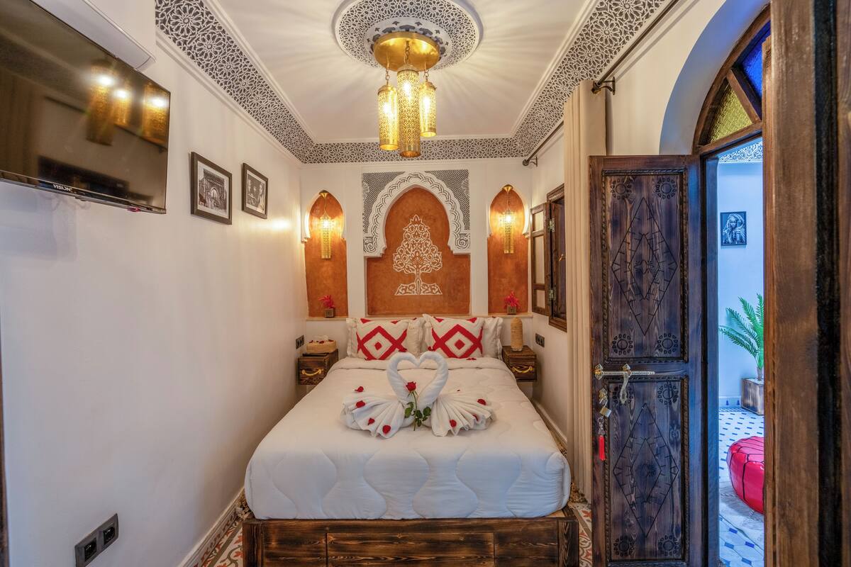 Una camera da letto ordinata con un letto, pannelli decorativi a parete, un lampadario e una porta in legno.