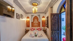 Quarto com cama, painéis decorativos na parede, um candelabro e uma porta de madeira.