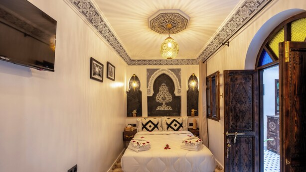 Quarto com uma cama grande, painéis decorativos na parede, uma televisão e um piso estampado.