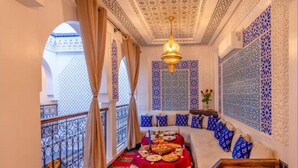 A room with a red carpet, a dining table set with food, a chandelier, and blue patterned walls. - Riad La Perle Bleue (Marrakech)