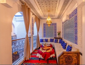 A room with a red carpet, a dining table set with food, a chandelier, and blue patterned walls. - Riad La Perle Bleue (Marrakech)