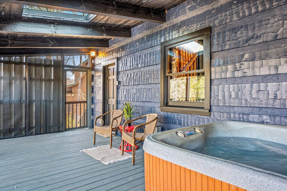 Una terraza de madera con un jacuzzi, sillas de mimbre y una pequeña mesa con una planta.