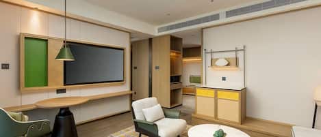 A modern hotel room with a flat-screen TV, a sofa, a round coffee table, and a patterned rug.