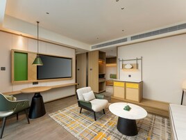Una habitación de hotel moderna con una televisión de pantalla plana, un sofá, una mesita de centro redonda y una alfombra estampada.