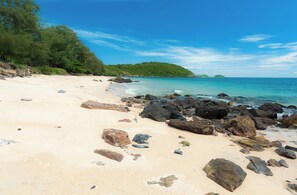 Une plage avec une eau turquoise et limpide, un rivage sablonneux et de gros rochers.