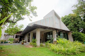 A modern building with a sloped roof, large windows, and a covered outdoor area with potted plants. - Koh Lanta Amantra Hostel - Women Only (Ko Lanta)