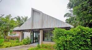 A modern building with a sloped roof, large glass windows, and a brick base. - Koh Lanta Amantra Hostel - Women Only (Ko Lanta)