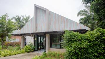 A modern building with a sloped roof and large glass doors, surrounded by lush greenery.
