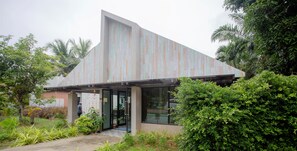 Un bâtiment moderne doté d’un toit en pente et de grandes portes vitrées, entouré d’une végétation luxuriante.