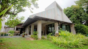 A modern building with a sloped roof, large windows, and a covered outdoor area with potted plants. - Koh Lanta Amantra Hostel - Women Only (Ko Lanta)