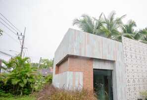 A modern building with a brick base and a wooden panel facade, surrounded by greenery and palm trees. - Koh Lanta Amantra Hostel - Women Only (Ko Lanta)