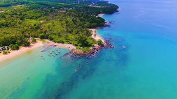 An aerial view of a coastal area with a beach, boats, and lush greenery.