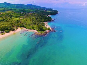 Vue aérienne d’une zone côtière avec une plage, des bateaux et une végétation luxuriante.