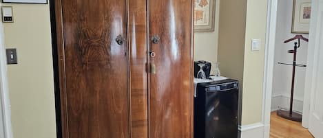 Una habitación con un armario de madera, una maleta negra, un tapiz estampado y una puerta que da a otra estancia.