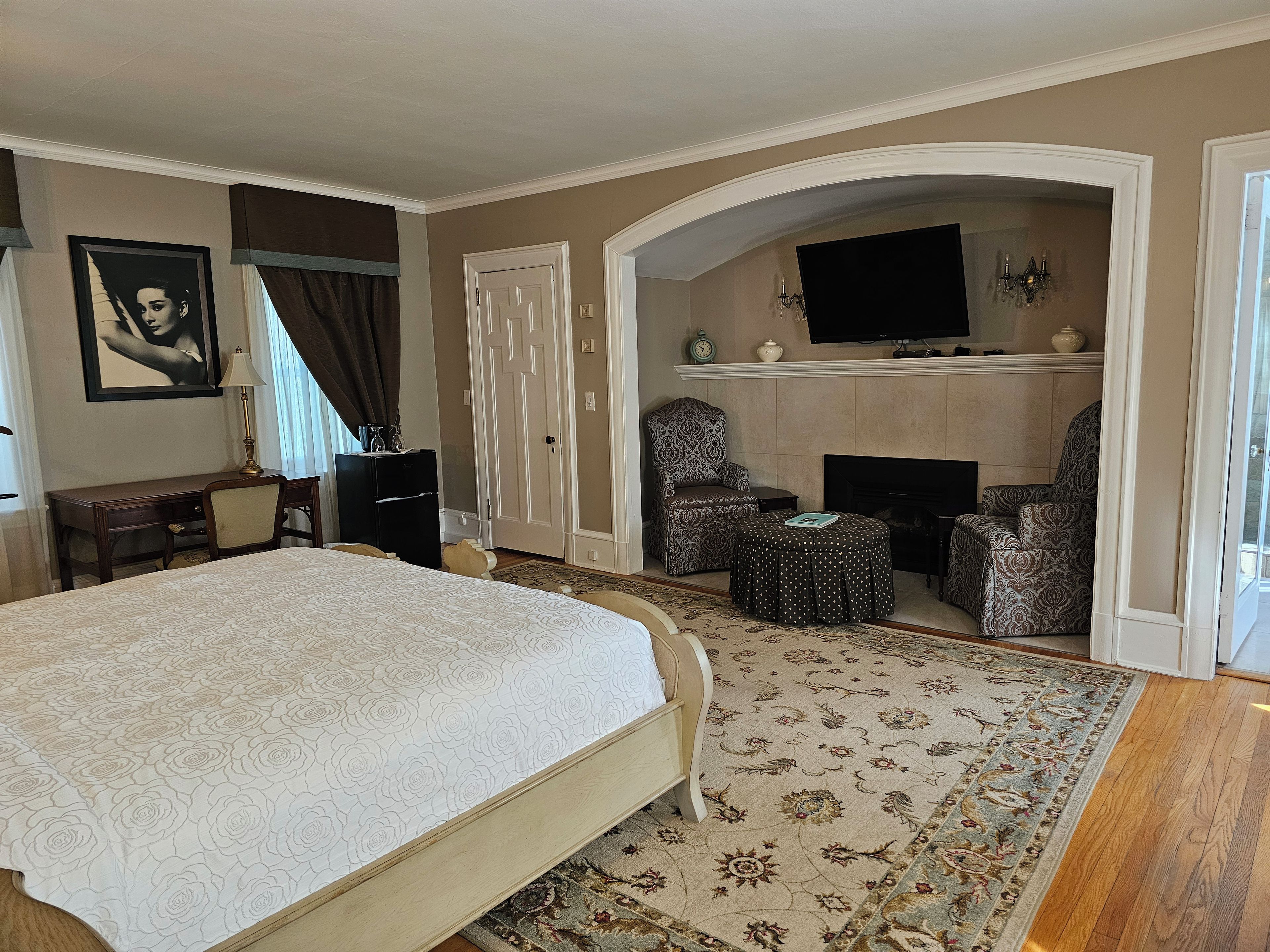 Ein Schlafzimmer mit einem großen Bett, einem Schreibtisch, einem Stuhl, einem Fernseher und einem Kamin.