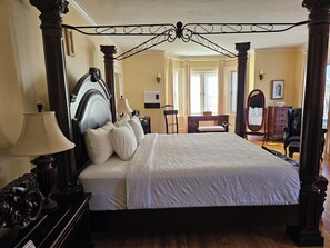 A four-poster bed with a dark headboard, a bedside table with a lamp, and a dresser with a mirror.
