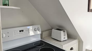Eine Küche mit einem weißen Herd, einem Toaster und einer kleinen Ablage mit einer grünen Flasche und Blumen.
