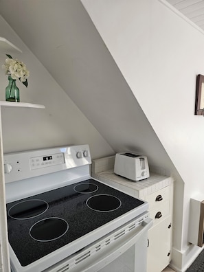 A kitchen with a white stove, a toaster, and a small shelf with a green bottle and flowers.