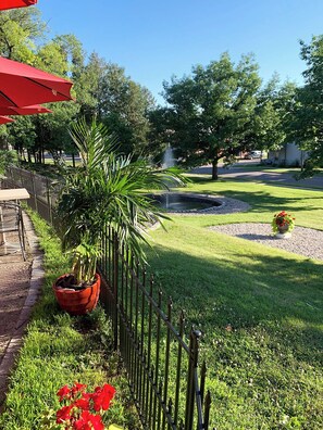 A well-maintained garden with a fountain, a red umbrella, and a metal fence.