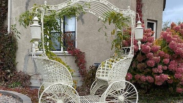 A white metal carriage with a basket, positioned in front of a house with a window and a door.