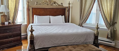 Un dormitorio clásico con una cama grande, un banco de madera, una mesita de noche y un rug con diseño.