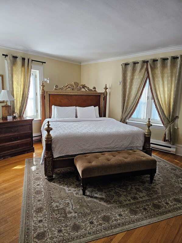 A classic bedroom with a large bed, a wooden bench, a nightstand, and a patterned rug.