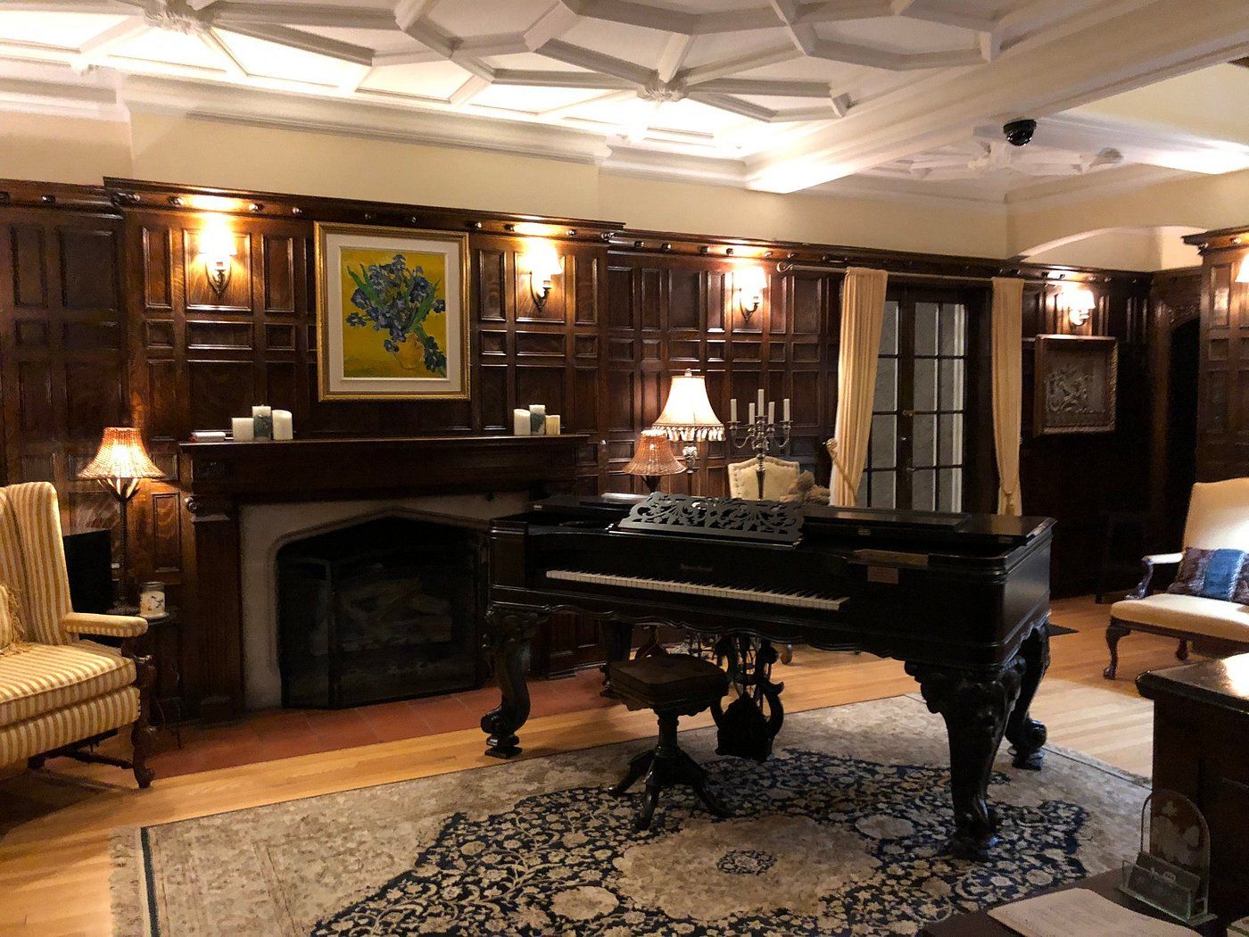 Une vaste pièce agrémentée d’un piano, de boiseries, d’une cheminée et d’un grand tapis.