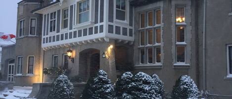 Une grande maison à plusieurs étages, dotée d’un porche avant imposant et d’un jardin recouvert de neige.