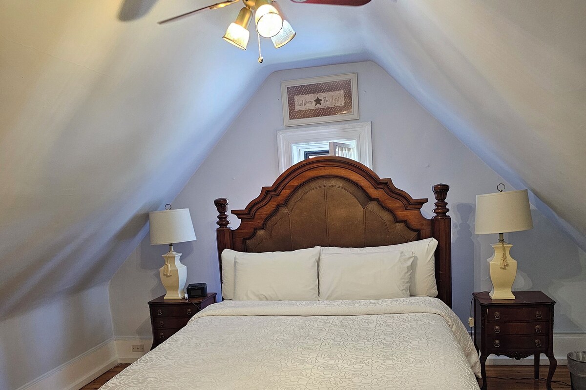 A bedroom with a wooden bed, two bedside tables with lamps, a ceiling fan, and a sloped ceiling.