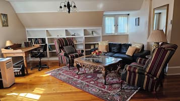 Ein Wohnzimmer mit Holzboden, einer schwarzen Ledersofa, gestreiften Sesseln, einem Glastisch und einem Bücherregal.