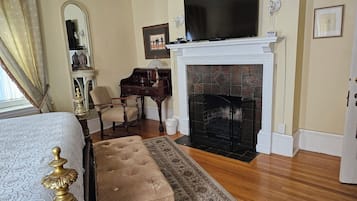 A bedroom with a bed, a desk, a chair, a fireplace, and a television.