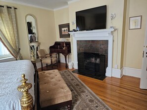 A bedroom with a bed, a desk, a chair, a fireplace, and a television.