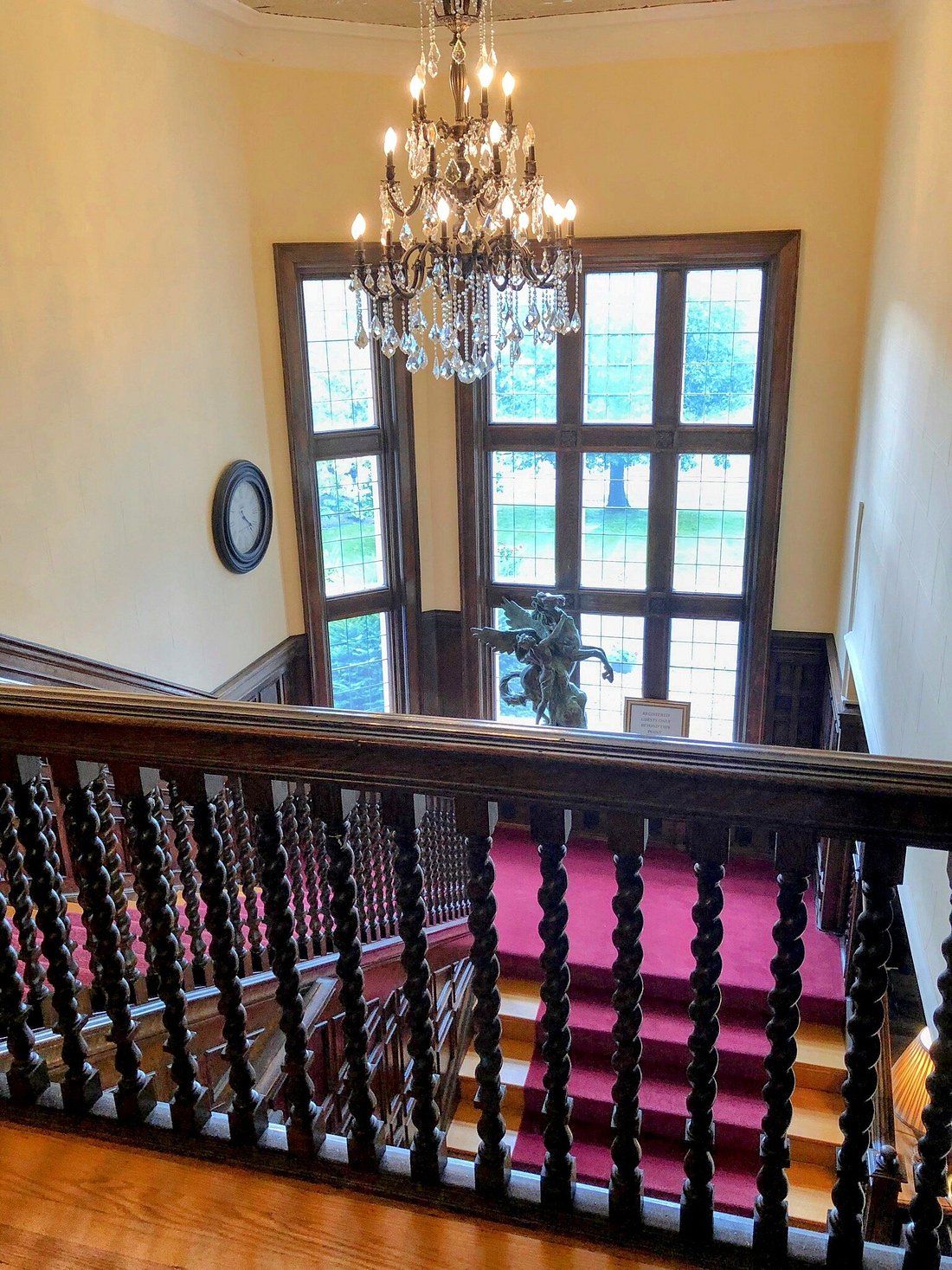 Una gran escalera con un candelabro, un reloj y vistas al exterior a través de amplios ventanales.