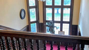 Una gran escalera con un candelabro, un reloj y vistas al exterior a través de amplios ventanales.
