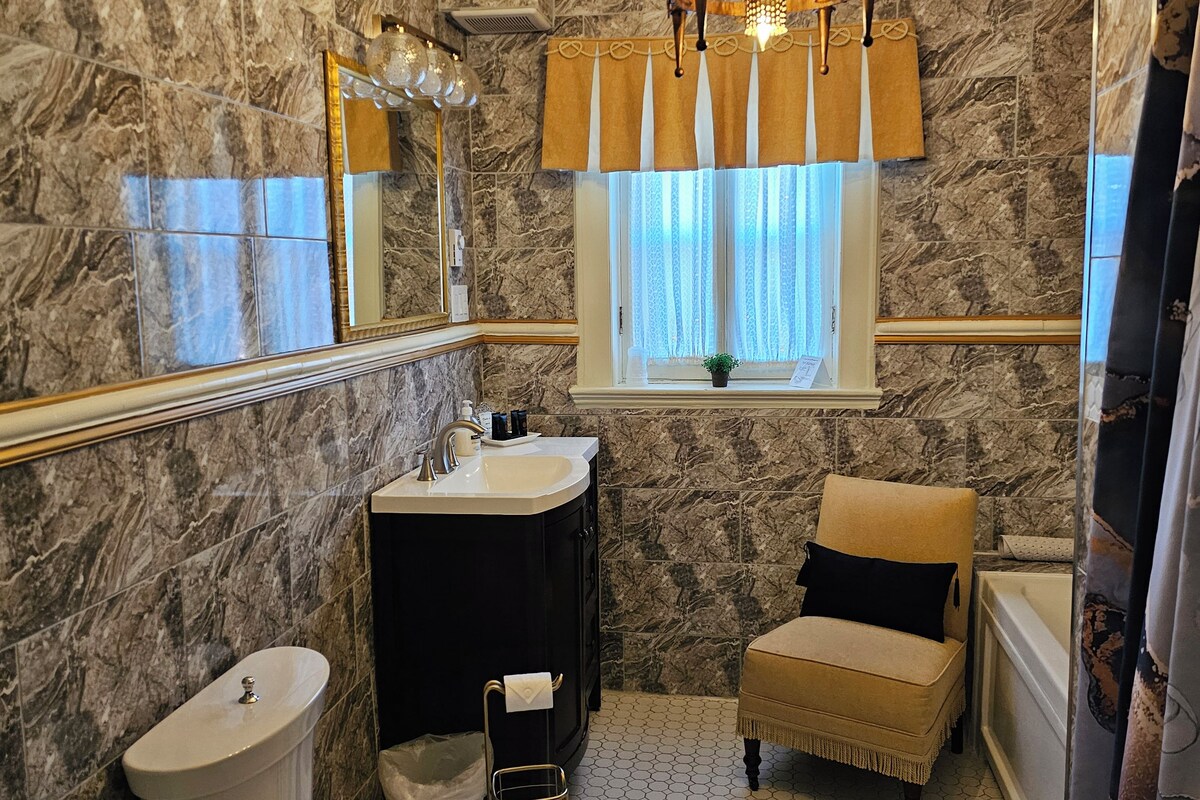 Un baño con pared de mármol, un lavamanos, un inodoro, una silla y una araña.