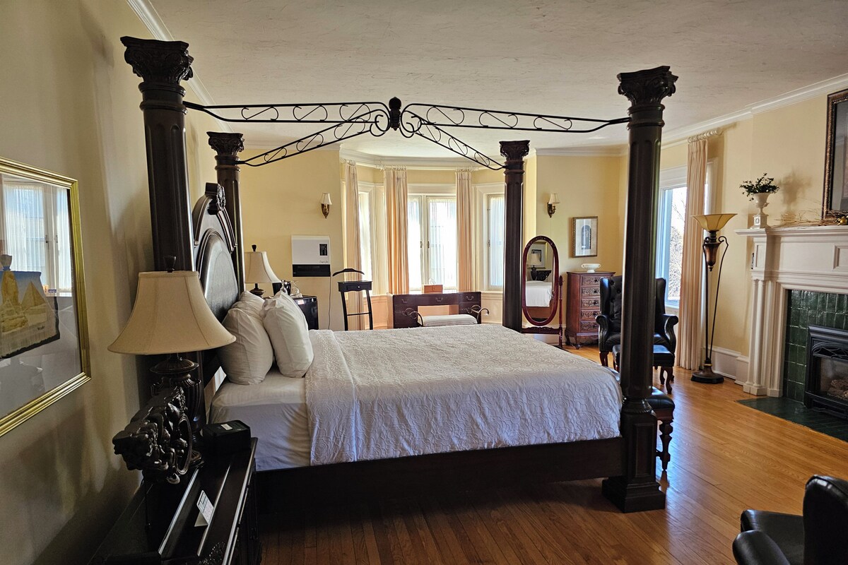 A spacious bedroom with a four-poster bed, wooden flooring, and a fireplace.